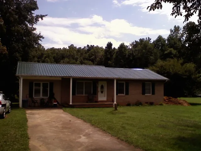 Dark green metal roof on a brick ranch with a covered porch in Sparta